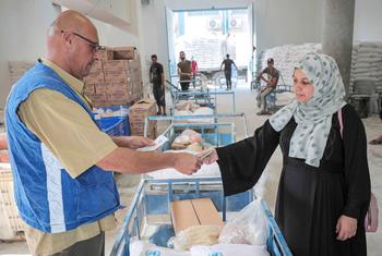 गाज़ा में UNRWA जबालिया वितरण केंद्र में एक फ़लिस्तीनी शरणार्थी महिला अपना भोजन सहायता पैकेज प्राप्त करते हुए.
