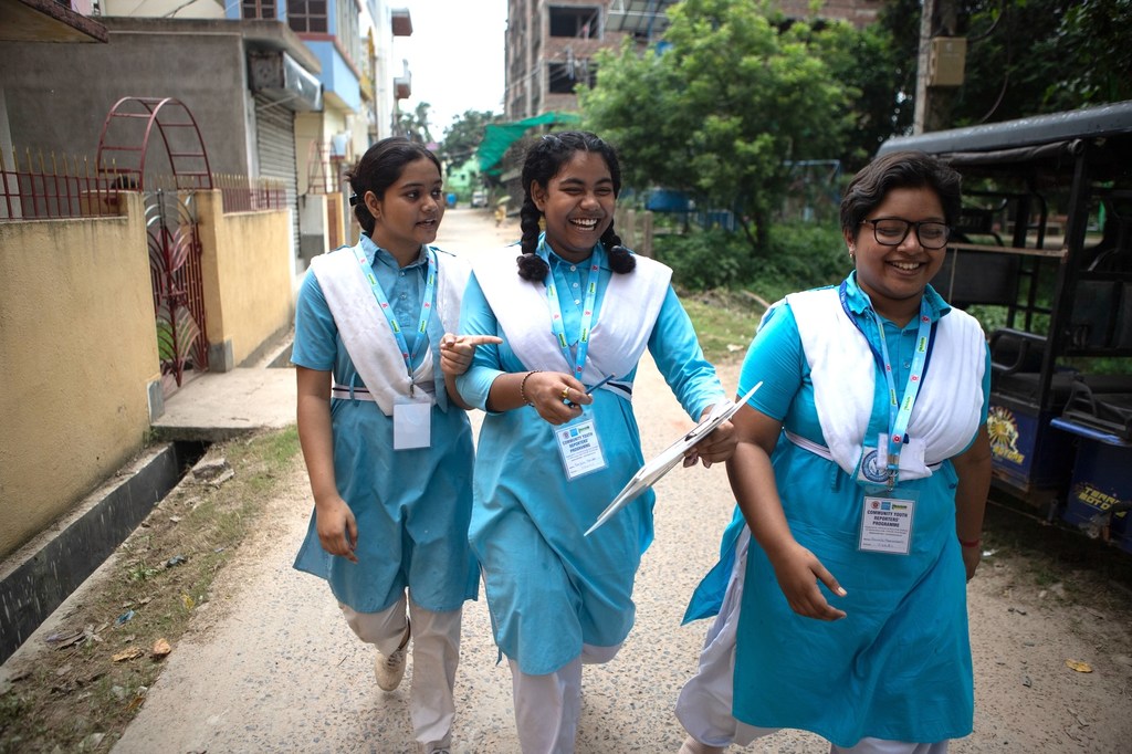नीली वर्दी और सफेद स्कार्फ पहने तीन युवतियां UNICEF यूथ रिपोर्टर कार्यक्रम में भाग लेते हुए एक सड़क पर चल रही हैं।
