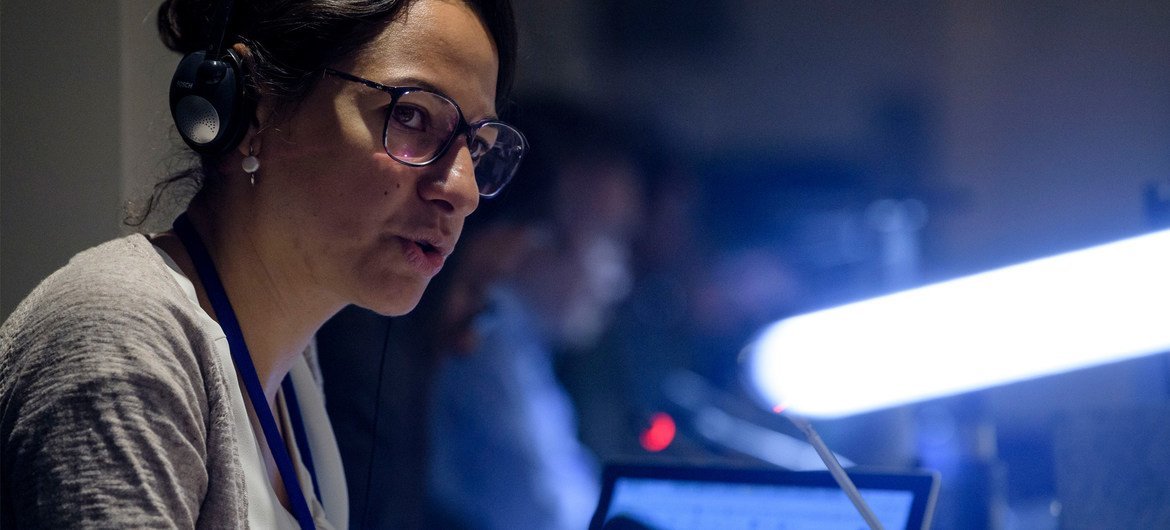 Una intérprete de la ONU , con auriculares y gafas, se encuentra frente a un micrófono en una conferencia.