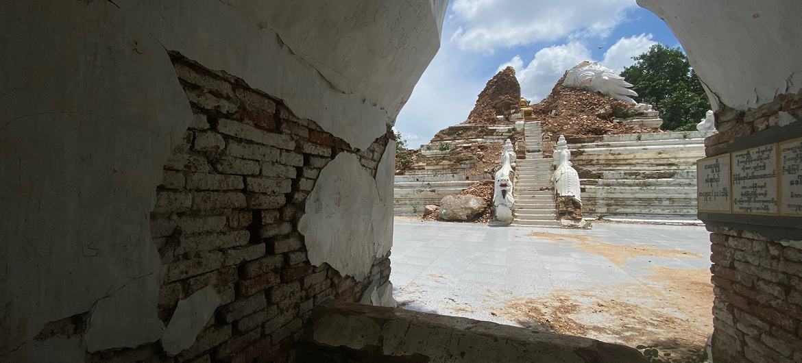 A view of a damaged pagoda in Mahaaungmyay, Myanmar, showing collapsed brickwork and exposed stone stairs under a blue sky.