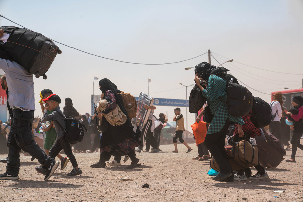 Los retornados afganos, incluidas mujeres y niños, cruzan la frontera de Islam Qala en la provincia de Herat, llevando sus pertenencias por un camino polvoriento. La ACNUR supervisa la situación mientras miles regresan desde Irán. Esta fotografía fue tomada el 24 de julio de 2025.