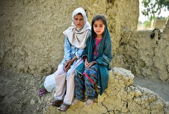 女孩们坐在泥屋受损的墙上，这座房子在2022年巴基斯坦的洪水中几乎被摧毁。
