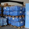 Suministros de ayuda humanitaria, incluyendo palés de bolsas azules y agua embotellada, se almacenan en un depósito en Panamá para su distribución tras el paso de los huracanes Eta e Iota. Se puede ver una pancarta con el logotipo de las Naciones Unidas .