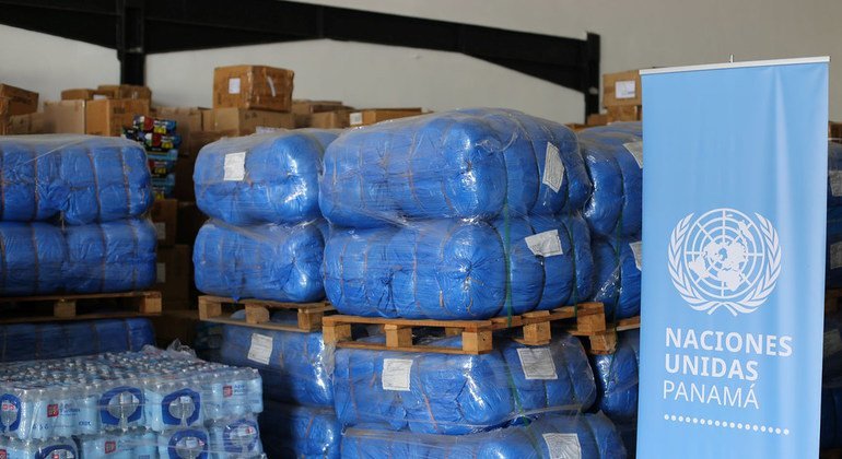 Suministros de ayuda humanitaria, incluyendo palés de bolsas azules y agua embotellada, se almacenan en un depósito en Panamá para su distribución tras el paso de los huracanes Eta e Iota. Se puede ver una pancarta con el logotipo de las Naciones Unidas .