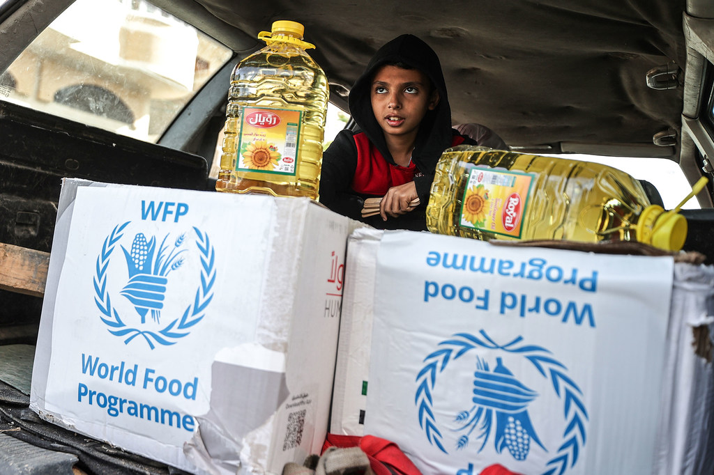 طفل يجلس في الجزء الخلفي من سيارة بجوار طرود غذائية تابعة لبرنامج الأغذية WFP وزجاجات زيت الطهي خلال عملية توزيع مواد غذائية في غزة.