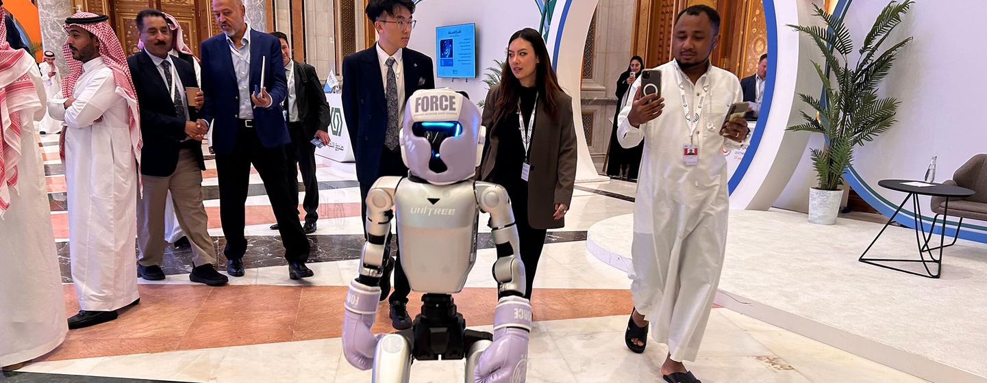 Un robot humanoide de Unitree Robotics se encuentra en un gran salón de la Cumbre Mundial de la Industria de la UNIDO 2025 en Riad, rodeado de asistentes.