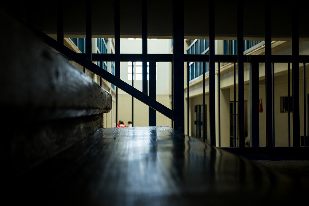 Una vista a través de los barrotes de una prisión hacia un patio donde se distinguen dos mujeres a lo lejos.