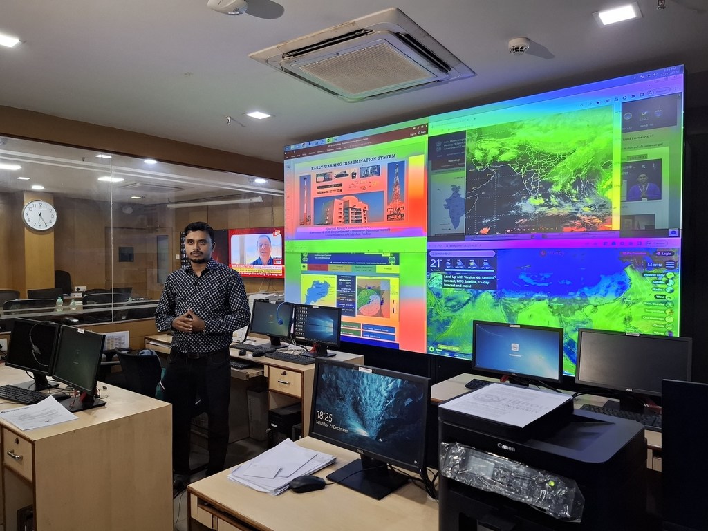 एक व्यक्ति नियंत्रण कक्ष में एक बड़ी स्क्रीन के सामने खड़ा है, जिस पर भारत के मौसम मानचित्रों के साथ एक प्रारंभिक चेतावनी प्रसार प्रणाली प्रदर्शित हो रही है।