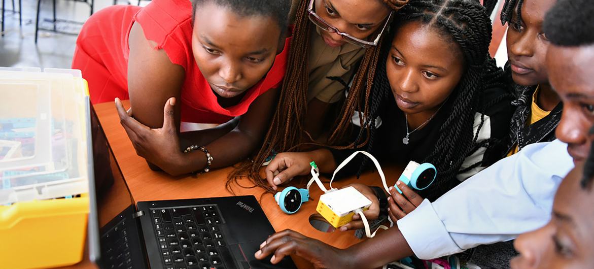 Un groupe de jeunes femmes sont réunies autour d'un ordinateur portable et d'un petit robot, travaillant sur un projet de robotique dans une salle de classe.