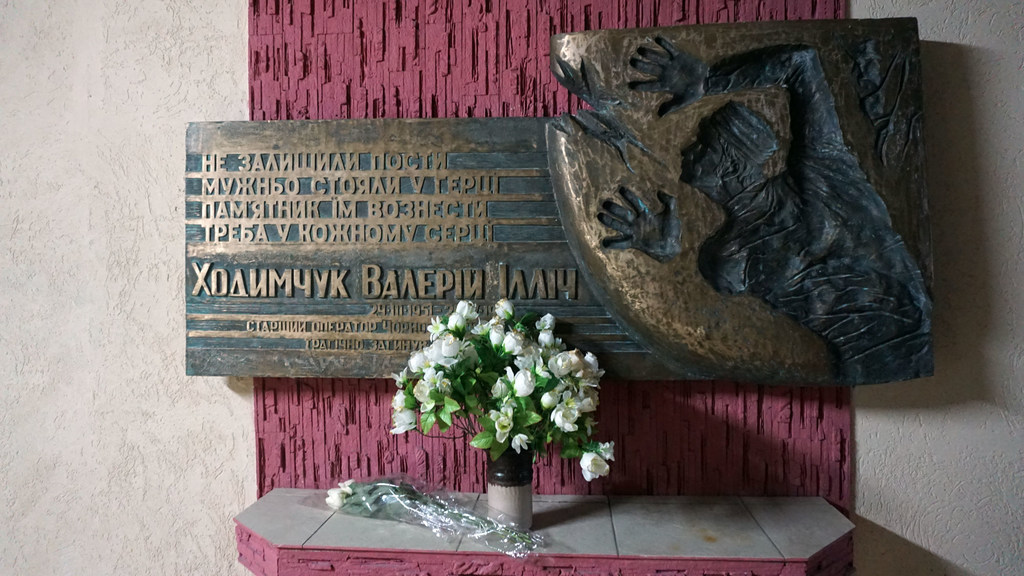 Bamba la ukumbusho lililowekwa kumbukumbu kwa Valeriy Khodimchuk, mkomeshaji wa Chernobyl, likiwa na mchoro wa shaba na vase ya maua meupe mbele yake.