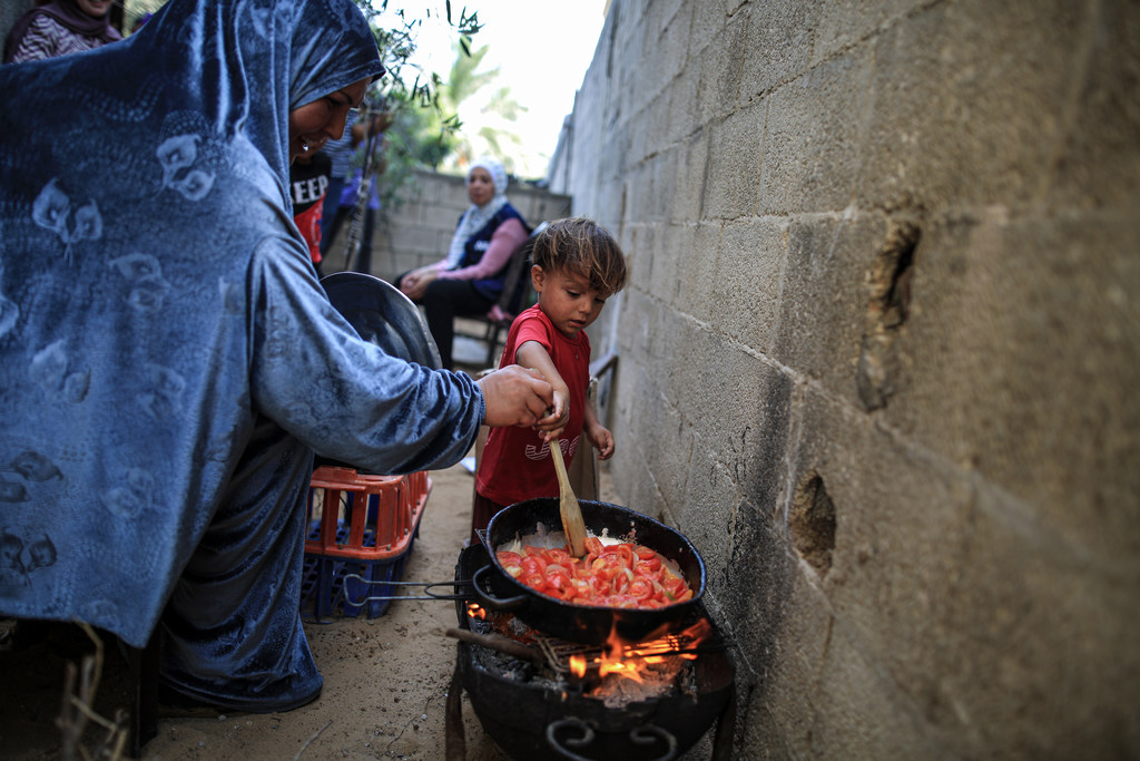 Amal y su pequeño preparan Shakshuka con tomates que compró en una tienda contratada por el PMA a través de su vale mensual.