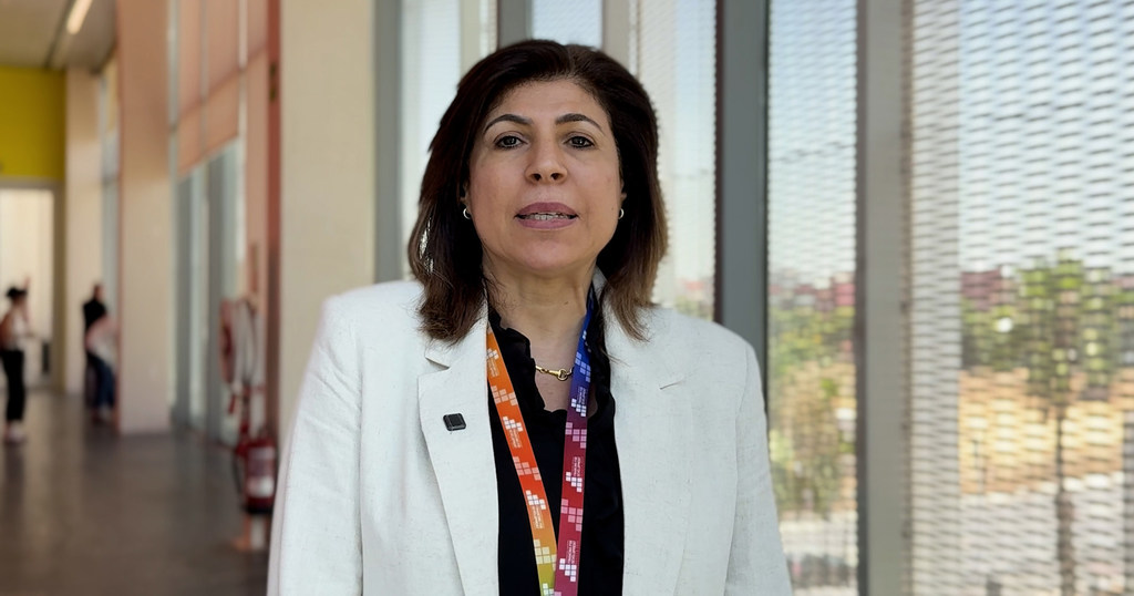 ندى العجيزي، مديرة التنمية المستدامة والتعاون الدولي في جامعة الدول العربية، ترتدي سترة بيضاء وحاملة بطاقات تعريفية للمؤتمر.