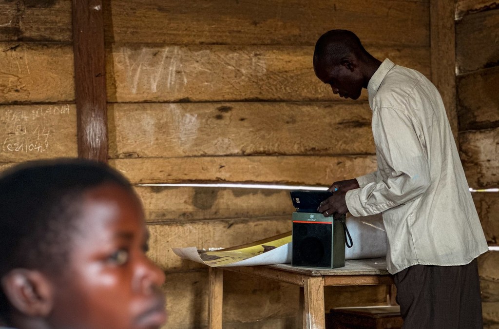 Mwalimu anarekebisha sauti ya spika iliyounganishwa na simu ya mkononi ili wanafunzi waweze kufuatilia kipindi cha elimu huko DRC. 