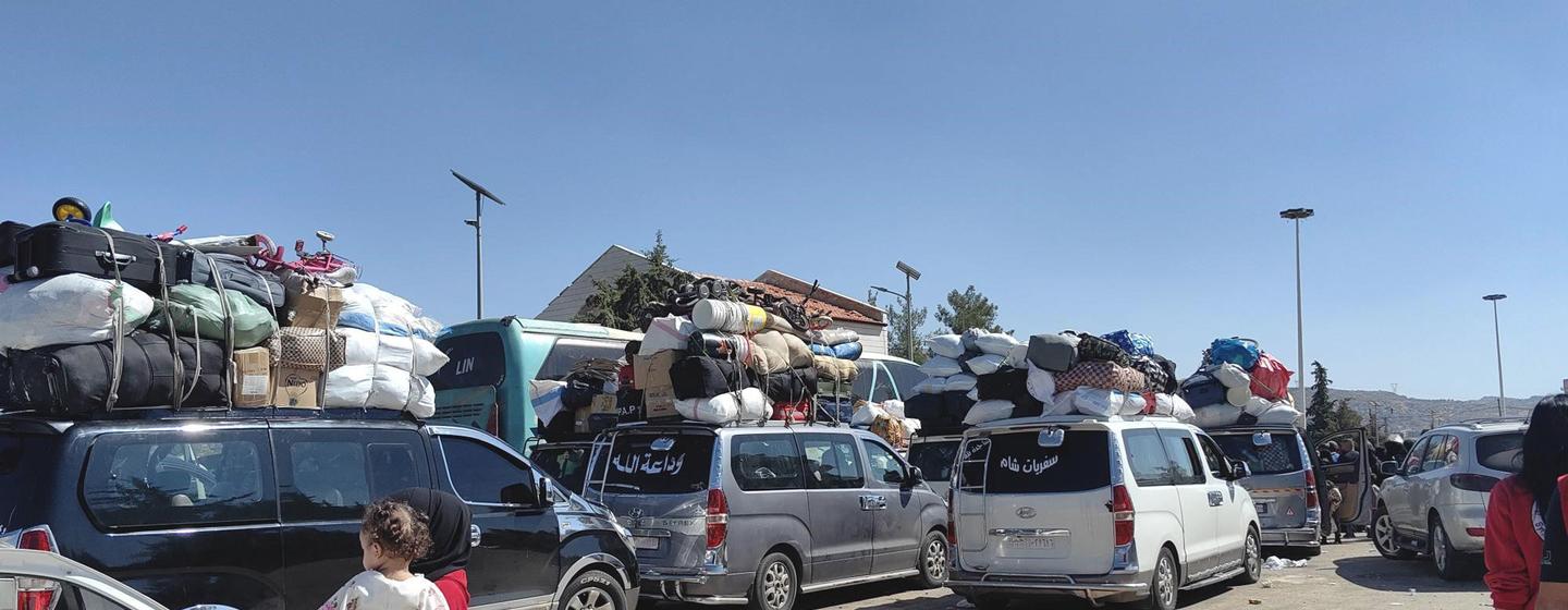 Des familles déplacées du Liban arrivent en Syrie en bus et en voiture à un poste frontière, emportant leurs biens essentiels.