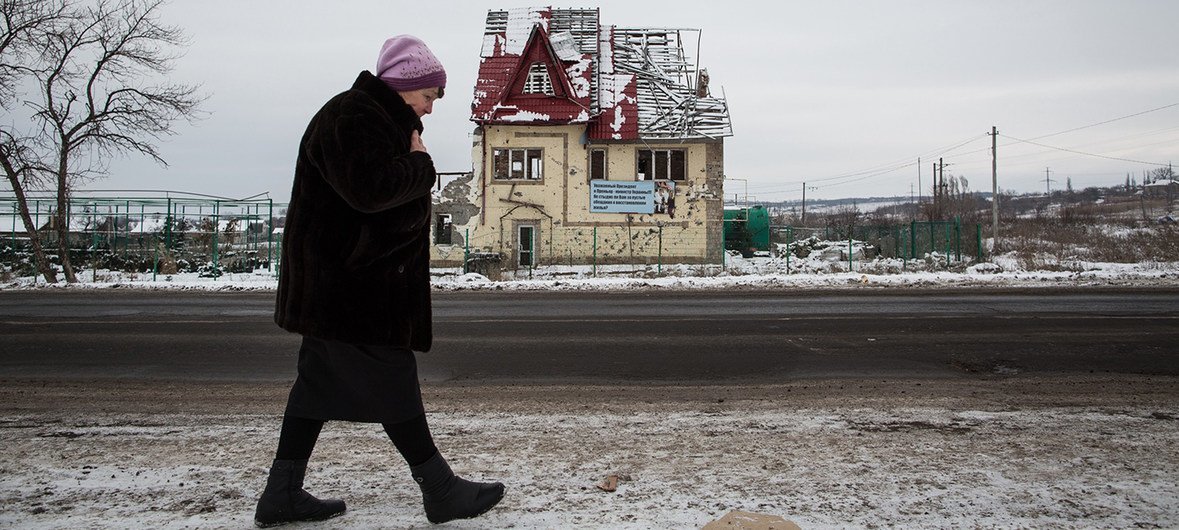 Une femme en Ukraine passant devant une maison en ruine
