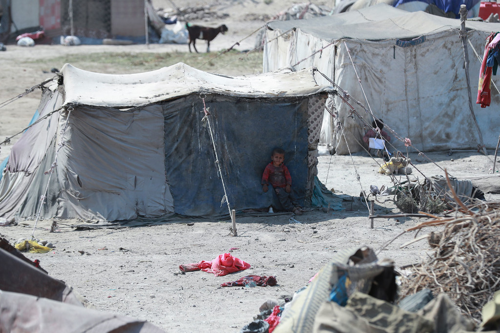 Uma criança pequena está sentada na entrada de uma tenda improvisada em um campo de refugiados no assentamento informal de Yawnani, em Raqqa, na Síria.