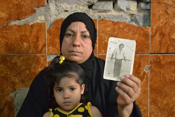 इराक़ में एक महिला 30 वर्ष पहले ग़ायब हुए अपने पति की तस्वीर दिखा रही हैं