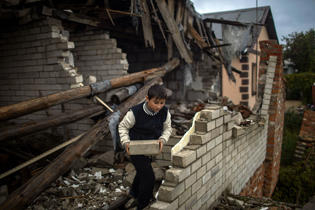 A nine-year-old boy helps his mother clear rubble from their heavily damaged home.