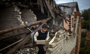 A nine-year-old boy helps his mother clear rubble from their heavily damaged home, in preparation for covering open areas with plastic as winter approaches.