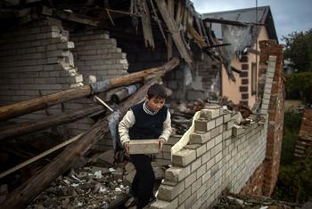 A nine-year-old boy helps his mother clear rubble from their heavily damaged home, in preparation for covering open areas with plastic as winter approaches.