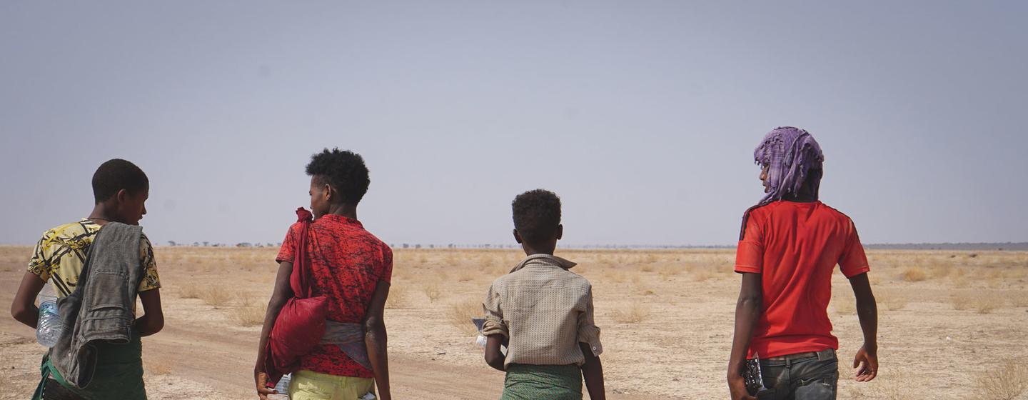 Quatre jeunes migrants éthiopiens marchent le long d'une route désertique à Djibouti, portant des cruches d'eau et leurs effets personnels.