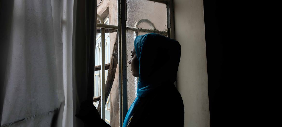 فتاة أفغانية صغيرة تقف كظلال عند نافذة، تنظر إلى الضوء.
