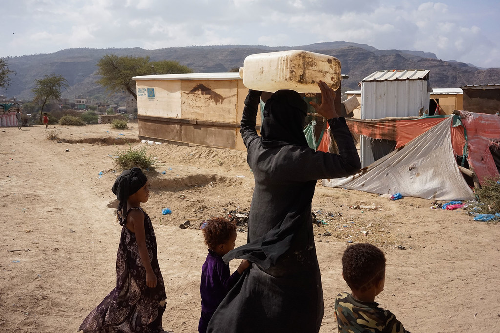 Una madre con sus hijos lleva agua a un refugio temporal en Taiz, Yemen.