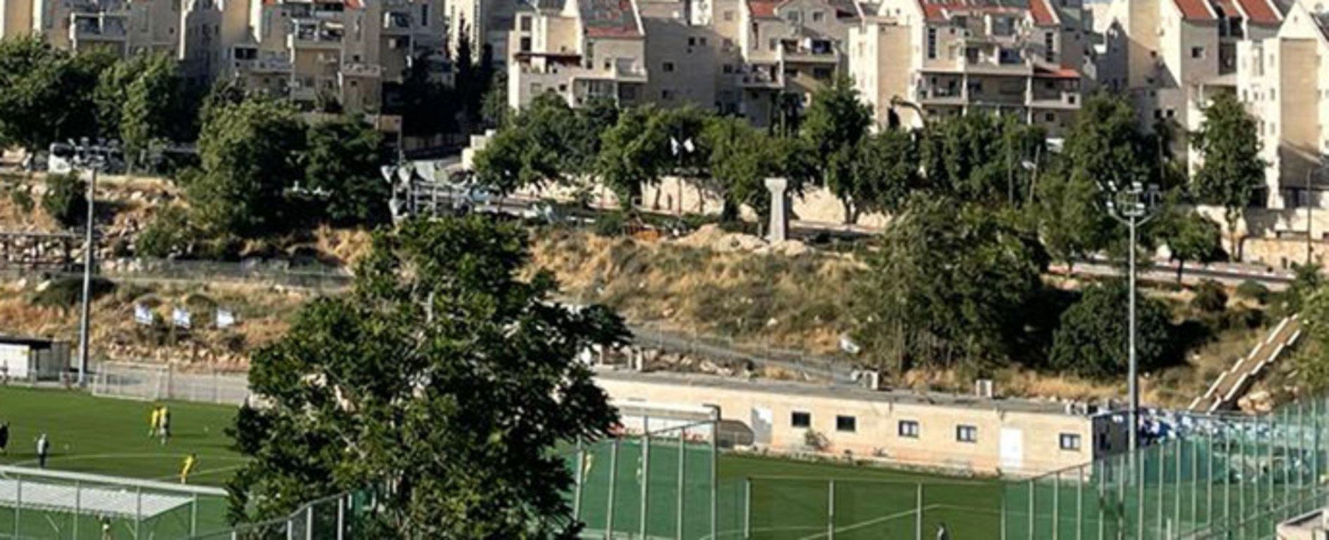 Un asentamiento residencial en Jerusalén bajo un cielo azul claro, con un campo de fútbol en primer plano.