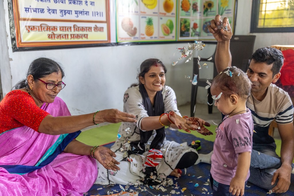 आंगनवाड़ी कार्यकर्ता, मीनाक्षी मांकर, नीलेश राठौड़ और उनकी पत्नी पूजा को उनके एक साल के बेटे विहान के साथ खेलने वाले खेल सिखा रही हैं.