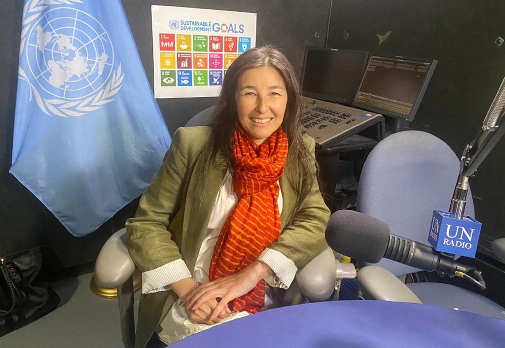Estelle Zadra, afisa mshirikishi wa UNESCO, anaonekana katika studio ya redio akiwa na bendera UN na kipaza sauti cha Redio UN .