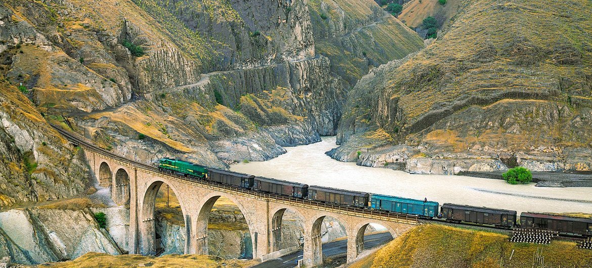 A train crosses a bridge as it makes its journey through a mountainous region.