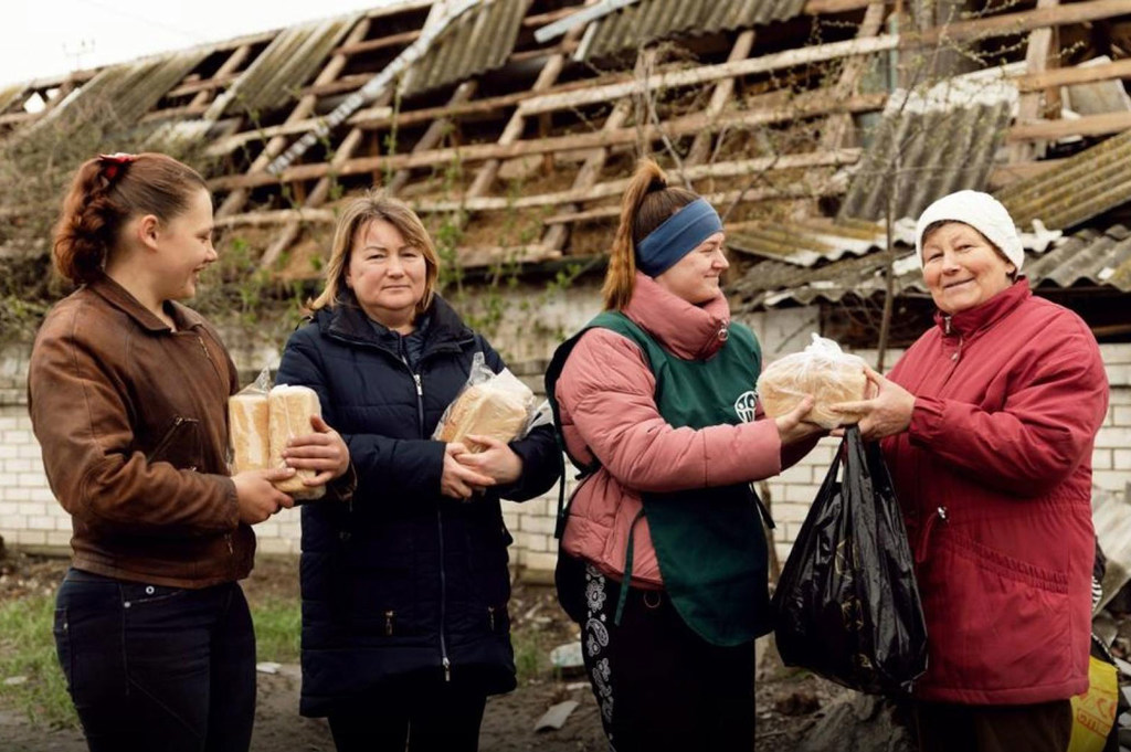 Trabajadores humanitarios reparten alimentos a civiles en Járkov, Ucrania, frente a un edificio dañado.
