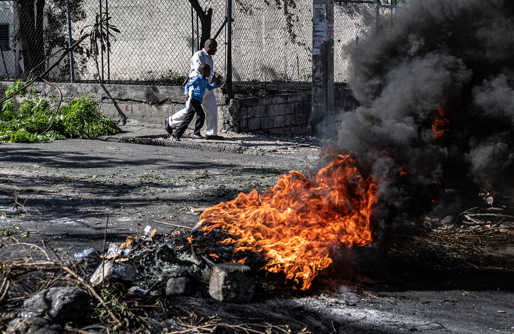 Un hombre camina con un niño junto a un gran incendio que arde en una calle de Puerto Príncipe, Haití.
