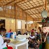 Uma profissional de saúde em uma clínica em Moçambique pesa um bebê em uma balança enquanto outras mães e crianças aguardam ao fundo.