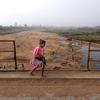 À Tsiombe, à Madagascar, une jeune fille vêtue d'une veste et d'une jupe roses traverse un pont au-dessus d'un lit de rivière complètement asséché, où les habitants creusent pour trouver de l'eau, une ressource rare en raison de la sécheresse.