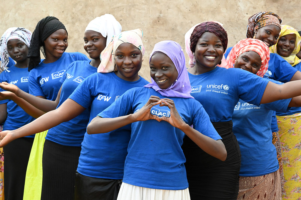 Kundi la wanawake vijana waliovaa shati la bluu UNICEF na KFW wakipiga picha nchini Chad. Mwanamke mmoja katikati anaunda umbo la moyo kwa mikono yake.