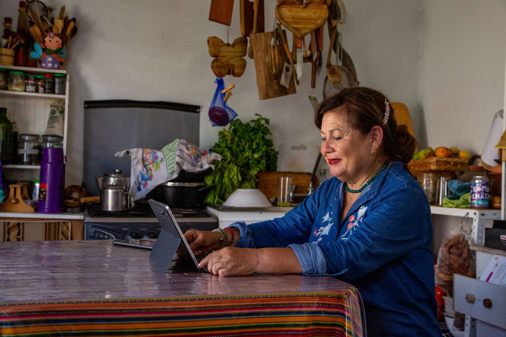 Una mujer mayor usa una tableta mientras está sentada a la mesa de la cocina.