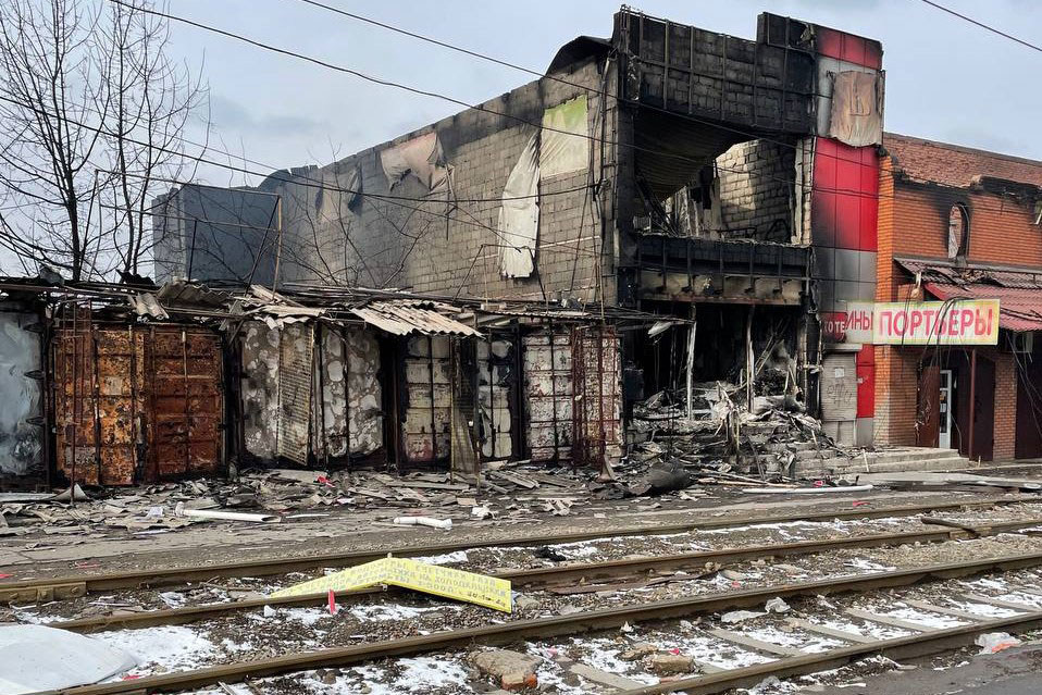 Сильно поврежденное и сгоревшее здание в Мариуполе, Украина, с обломками, разбросанными по земле возле железнодорожных путей.