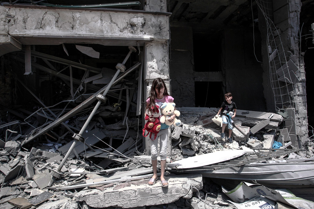 Una niña y un niño palestinos permanecen de pie entre los escombros de un edificio dañado en la ciudad de Gaza.