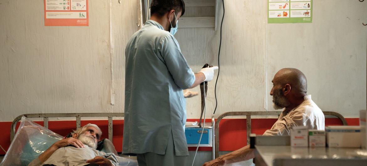 Um médico do sexo masculino, vestindo uniforme azul claro e máscara, atende pacientes idosos no Centro de Tratamento de Drogas Avicena, em Cabul, Afeganistão.