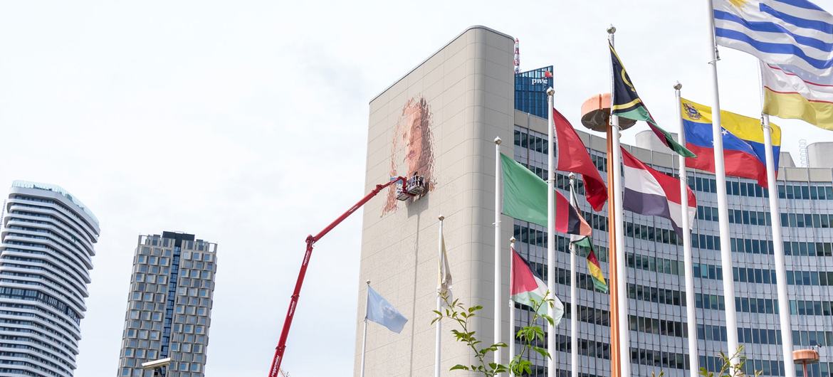 Street artist Fintan Magee high atop a cherry picker creating the mural at the Vienna International Centre.