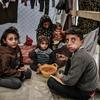 Uma família é vista sentada ao redor de uma tigela de feijão em sua tenda em Rafah, no sul da Faixa de Gaza.