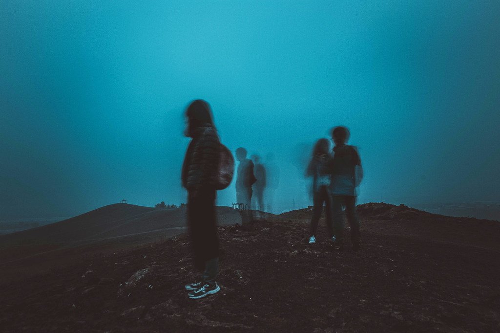 Un grupo de excursionistas se encuentra en una cresta montañosa neblinosa, capturado con una larga exposición que genera un efecto de desenfoque de movimiento.