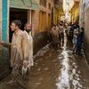 شلوار قمیض میں ملبوس مرد مون سون کے موسم میں پاکستان کے ایک رہائشی علاقے میں سیلابی، کیچڑ والی گلی سے گزر رہے ہیں۔