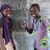 Watoto wawili wenye tabasamu, msichana na mvulana, wamesimama darasani mbele ya ubao huko Bol, Chad. Mvulana ameshika kipande cha chaki.