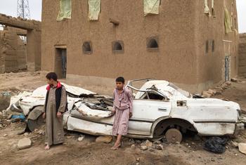 也门萨达，两个男孩站在一辆损坏的汽车前。