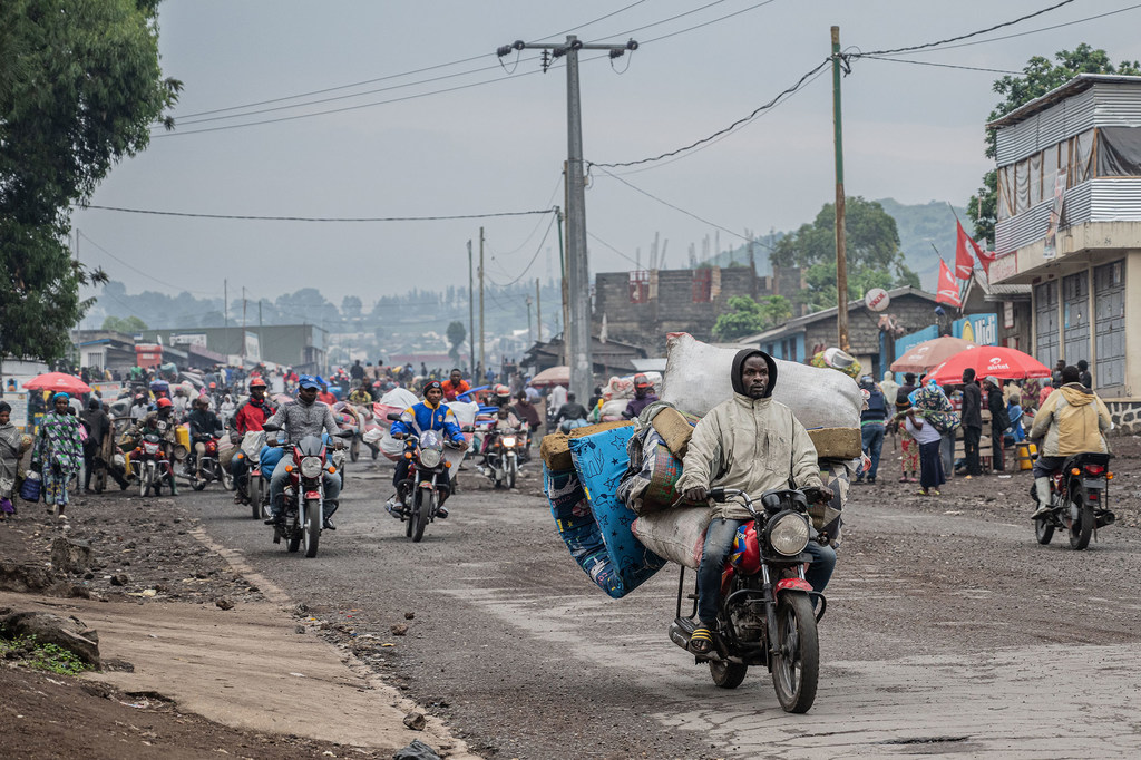Watu waliokimbia makazi yao wanakimbia kutoka kambi ya wakimbizi wa ndani karibu na Goma, DRC, huku baadhi yao wakiendesha pikipiki zilizojaa kupita kiasi kando ya barabara iliyojaa watu.