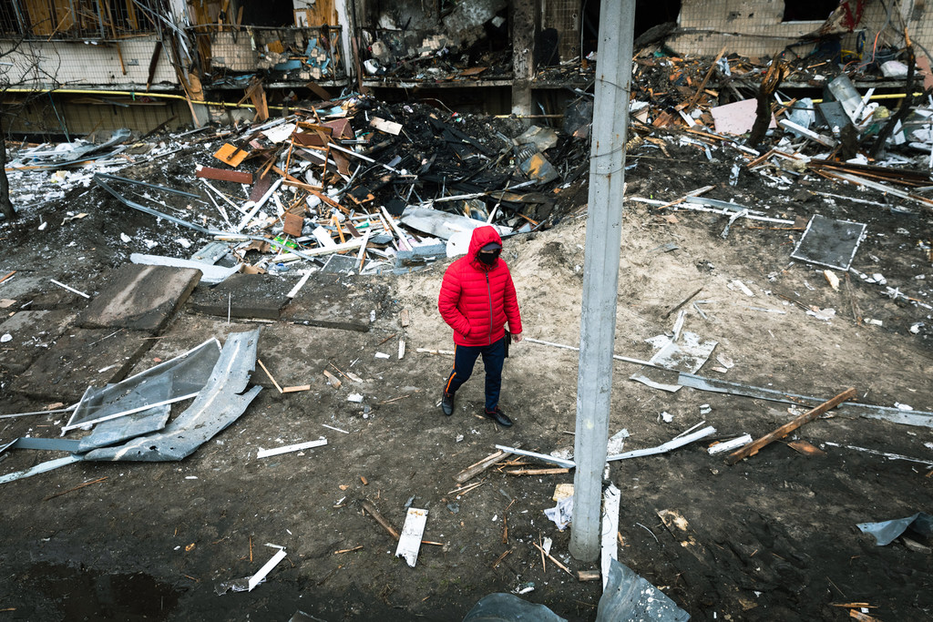 Un hombre con una chaqueta roja con capucha camina a través de un cráter y los escombros dejados por una explosión en Kiev, Ucrania.
