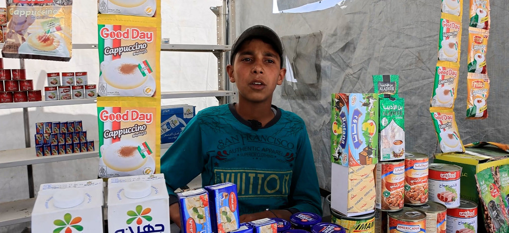 تقف براء أبو عائشة، وهي طفلة فلسطينية، خلف متجر بقالة صغير أقيم داخل خيمة في مدينة غزة.