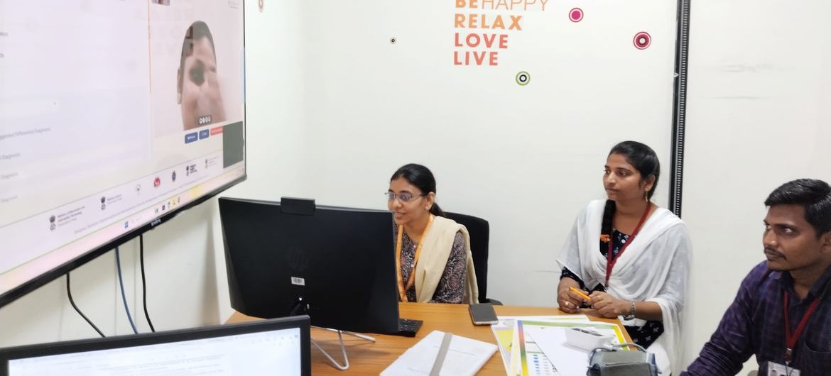 कक्षा में बैठे तीन वयस्क एक बड़ी स्क्रीन पर वीडियो कॉल देख रहे हैं, जो संभवतः UNICEF इंडिया की बाल मानसिक स्वास्थ्य संबंधी सखी पहल के लिए है।